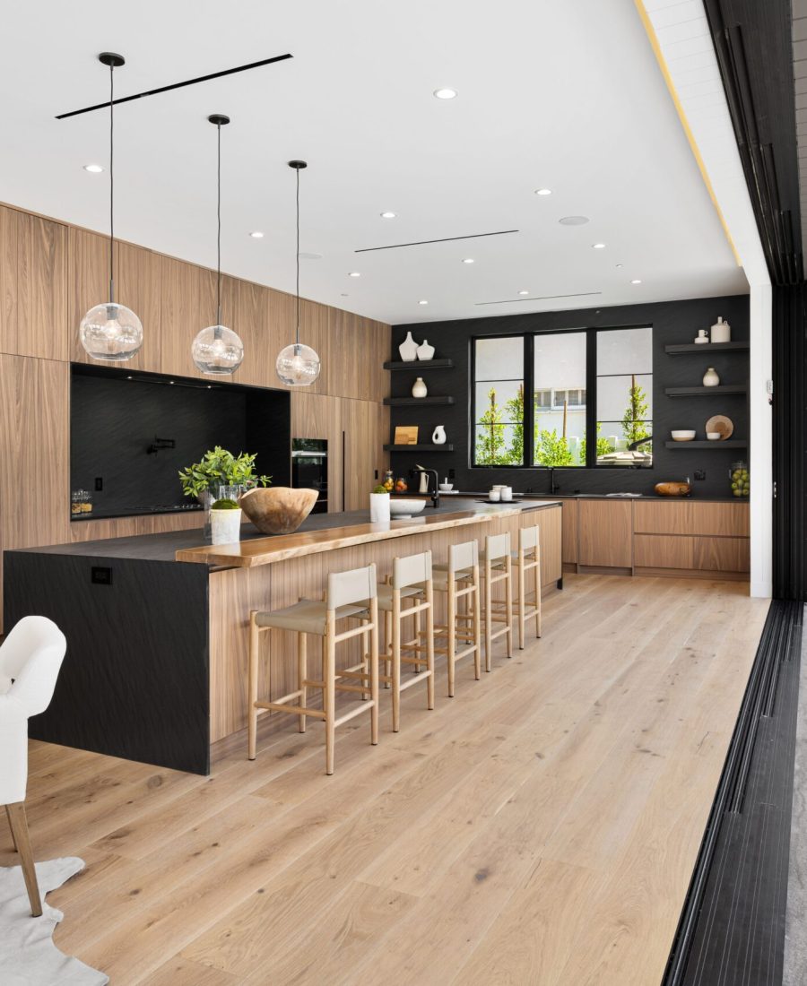 Modern open-concept kitchen with wooden cabinets, large island, and floor-to-ceiling windows leading to an outdoor patio.